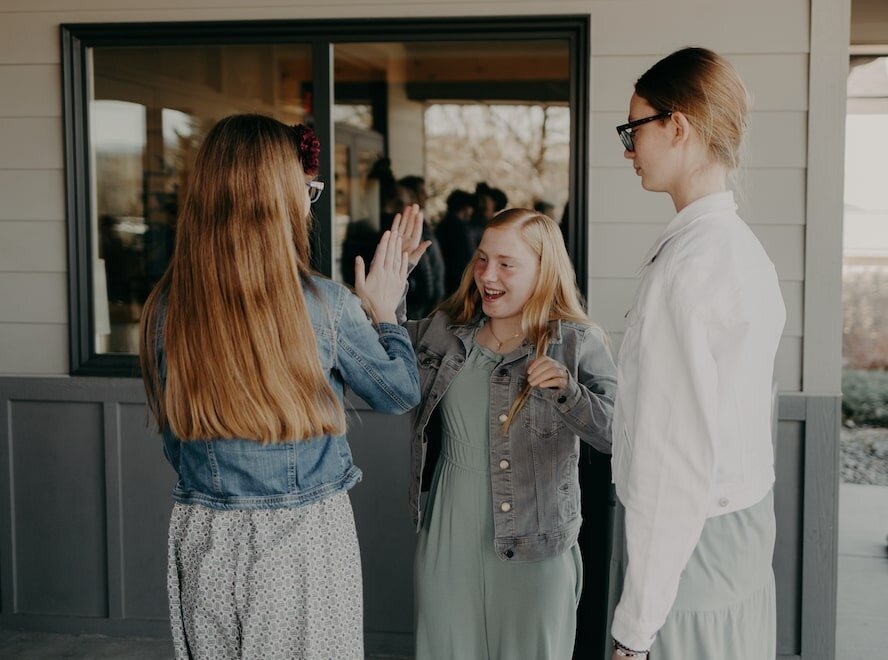 Two girls give each other a high five outside of Emmaus Road Church in Bozeman, MT while another girl looks on